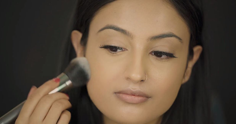 Woman applying Vasanti Face Base Powder Foundation on her cheeks - on black background