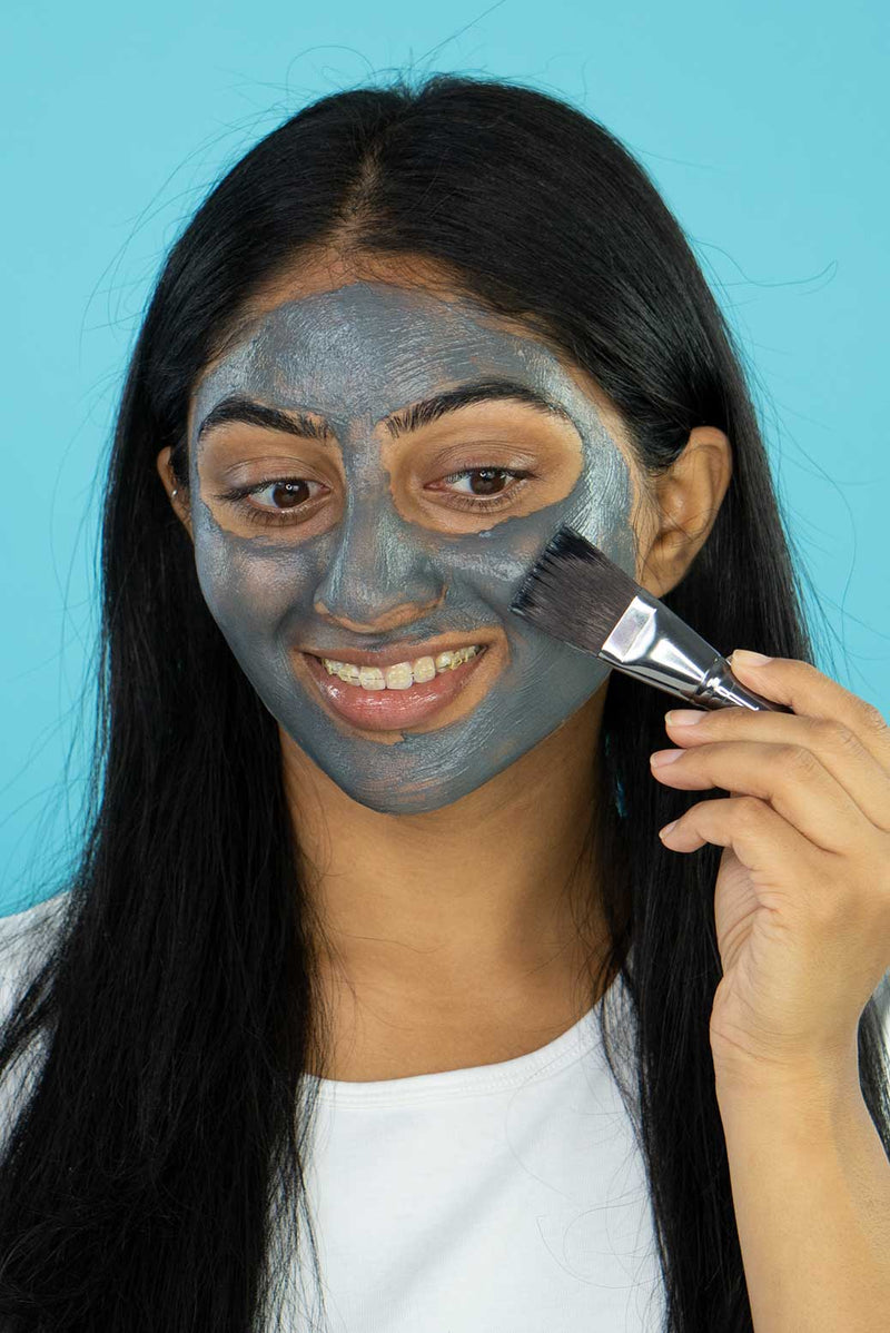 A girl applying Vasanti Brighten Up! Miracle Mask on her face using Vasanti Stubby Miracle Mask Brush